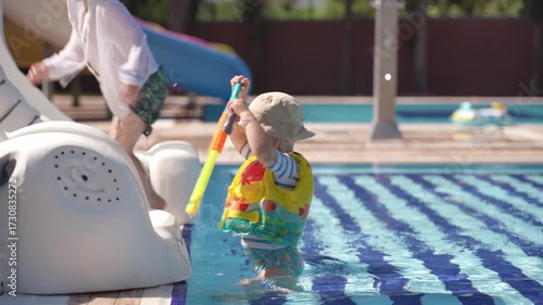 A happy little boy is enjoying himself in the pool. He is playing with a water gun and shooting at his younger brother.