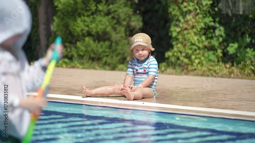 A happy little boy is enjoying himself in the pool. He is playing with a water gun and shooting at his younger brother.