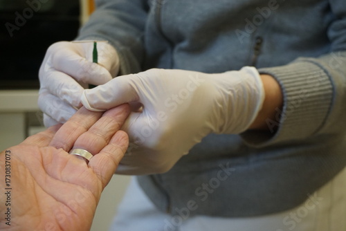 Ärztin mit weißen medizinischen Handschuhen hält Hand von Patientin mit stick zum Blutzuckermessen in Arztpraxis