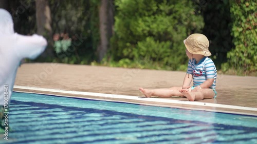 A happy little boy is enjoying himself in the pool. He is playing with a water gun and shooting at his younger brother.