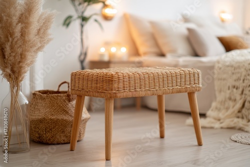 A light-brown wicker footstool sits in a bedroom, accented by a beige color palette and natural elements.