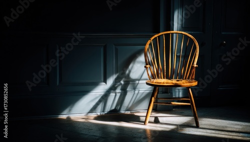 A wooden Windsor chair bathed in dramatic sunlight casts a strong shadow within a dark, paneled room.