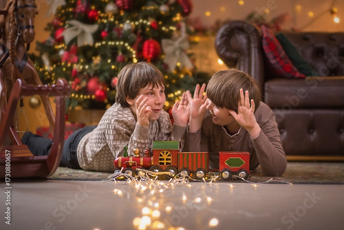 two boys are having fun playing with a train under a Christmas tree