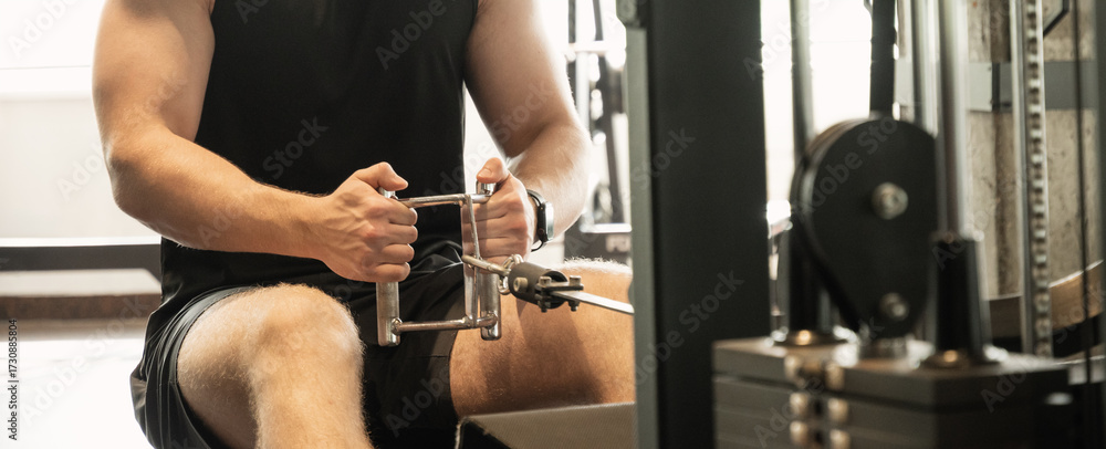 Fototapeta premium Young caucasian man wearing blank sleeveless tank top exercising on low rowing machine at gym. Banner. Close up.