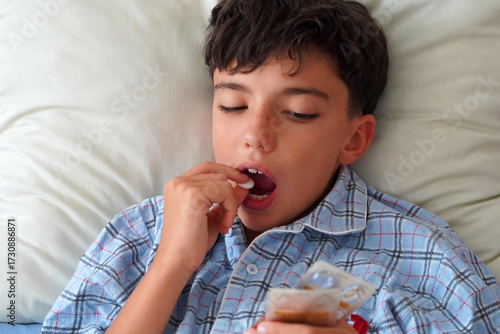 child in pajamas sick in bed taking a cough pill