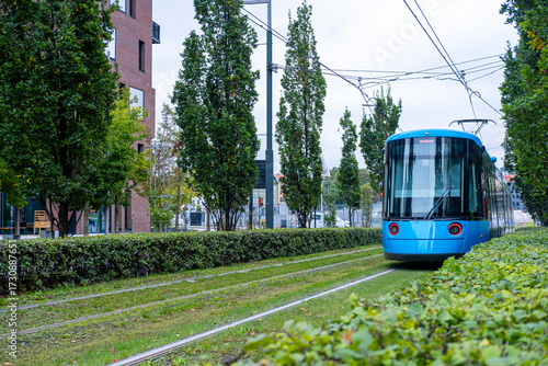 Blue tram on green track surrounded by trees in Oslo, clean energy public transport and sustainable mobility