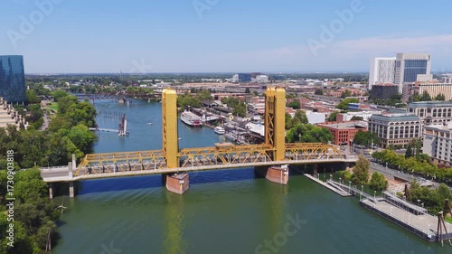 Aerial view of Sacramento, California, featuring the golden Tower Bridge, Sacramento River, downtown skyline, and boats along the riverbank.