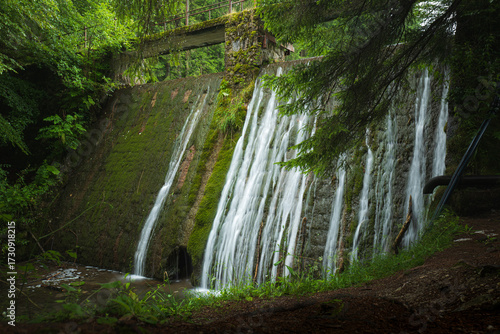 Small forest dam with stone wall and cascading waterfall streams in peaceful woodland