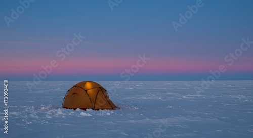 Orange tent with light inside on remote snowy landscape at sunset. Winter camping and survival in extreme conditions.