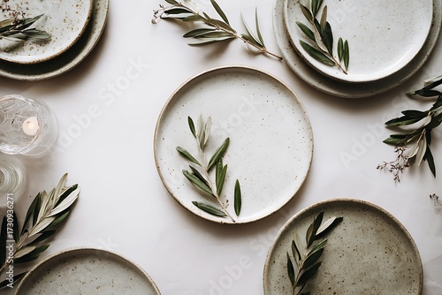 A serene flat lay composition featuring rustic ceramic plates adorned with fresh olive branches and a warm candle glow.