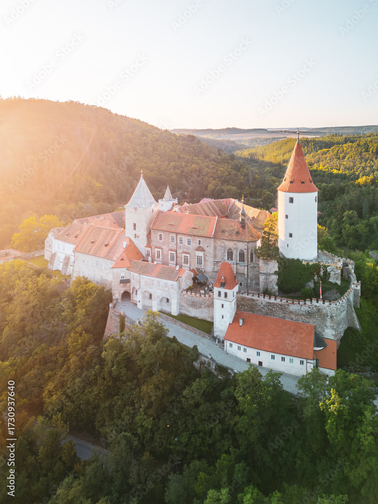 Obraz premium Krivoklat Castle stands majestically in Central Bohemia, showcasing its medieval architecture during a stunning sunset. The vibrant colors highlight its historic features against lush greenery.