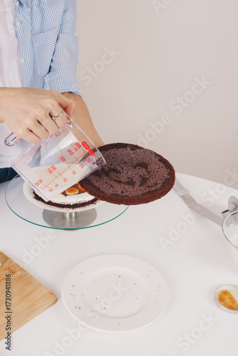 Young woman with slim hands filling a chocolate sponge cake with milk on a special stand. Home made chocolate sponge cake, traditional cooking, young housewife.