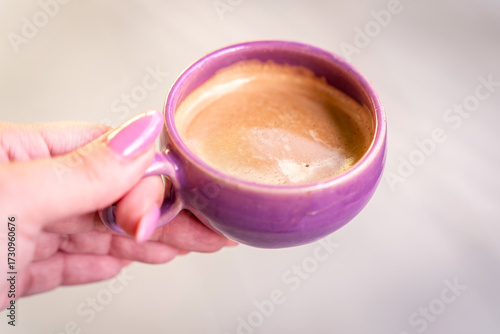 Espresso coffee in a small lilac mug. woman holding a ristretto isolated on off-white bg