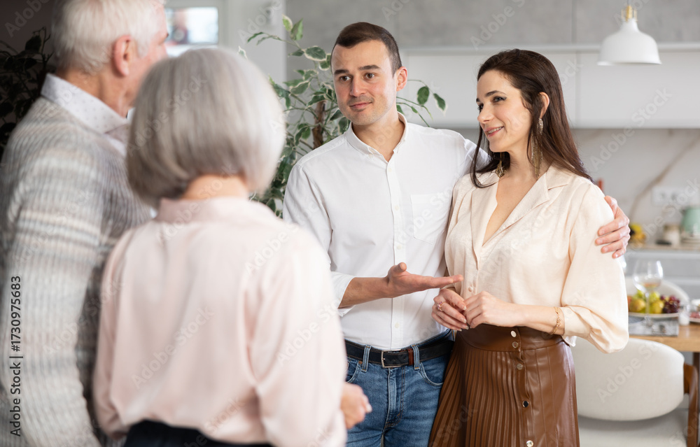 Fototapeta premium Adult man introduces his beloved girlfriend to elderly parents. Perplexed senior spouses are upset by new acquaintances, they look disapprovingly at their son and his female partner