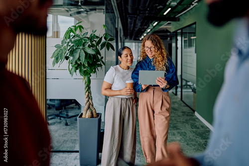 Fotografie Two business women standing in an office corridor collaborating and discussing w