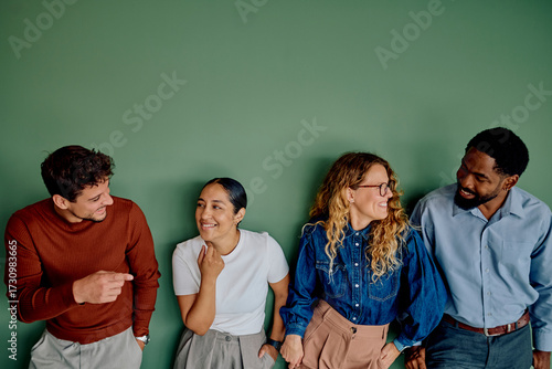 Diverse group of colleagues smiling and casually talking, standing together against a plain green wall
