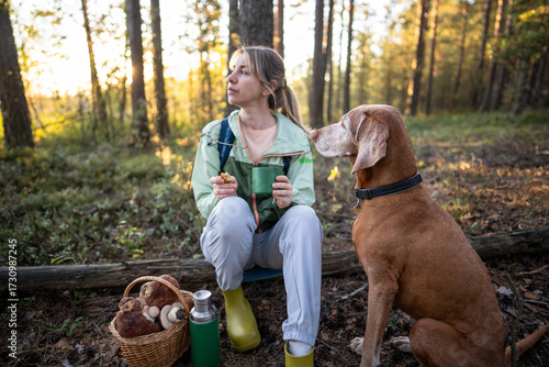 Canvas-taulu Pensive dreaming woman drinking tea in forest with attentive dog sitting close by