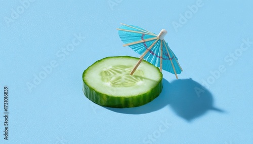 A vibrant, light-blue background showcases a cucumber slice, centrally positioned, with a miniature paper umbrella