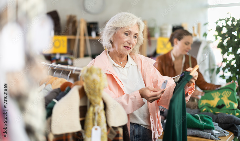 Obraz premium Elderly woman buyer choosing warm dress in clothing store