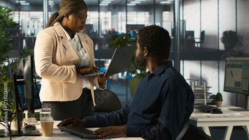 Worker in office receiving feedback from management executive looking over work done on laptop. African american manager in workspace giving tasks to employee, providing necessary data, camera A