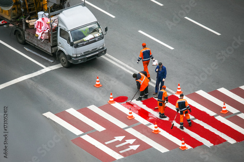 Workers paint new red pedestrian crosswalk on busy city street during daytime