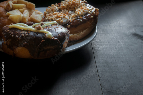 surtido de donas glaseadas en un plato blanco sobre una vieja mesa de madera con luz tenue y a contraluz. Copy space