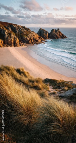 Coastal beach scene at dawn.  Golden light bathes a pristine, sandy beach.  Rolling waves meet the shore, with rocky cliffs beyond