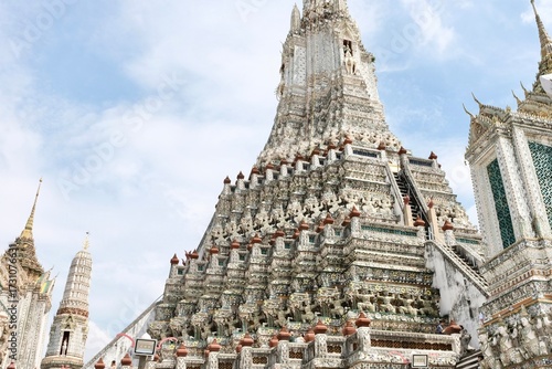 Low-angle view of the base of a prang at Wat Arun, the Temple of Dawn, featuring mythological figures from the Ramakien (Ramayana) and decorative porcelain shard mosaic tiles in a floral motif 