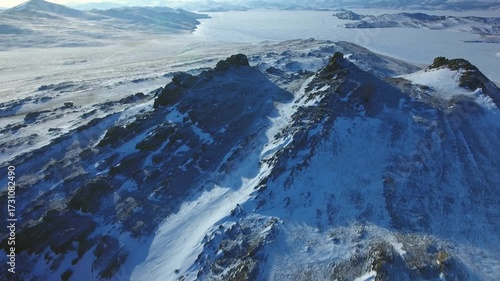 Helicopter epic above dark volcanic rocks covered with snow on frozen Lake Baikal. Endless ice, Siberian winter, amazing Northern nature. Islands and rocks vast landscape, breathtaking coastal scenery