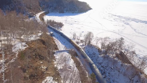 From above authentic old train on winter railway journey along frozen Lake Baikal, Siberia. Locomotive travels through snowy rural landscape near Listvyanka, abstract railroad tracks. Travel tour. 4k