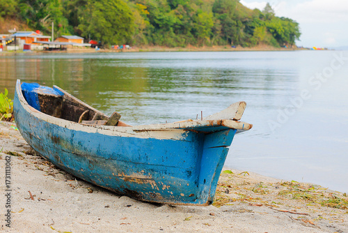 Fotografía Foto perahu kayu biru yang terdampar di tepi danau dengan suasana perkemahan di latar belakang