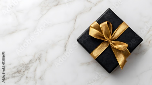 A black gift box with a golden ribbon and bow on a white marble background