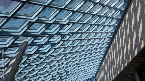 Low angle view of repeating pattern of windows along the large sloping surface of the roof with blue sky and sunlight visible. 