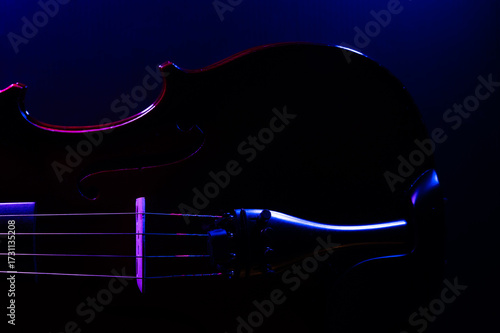 A violin on a dark background, side lit with purple and blue lights