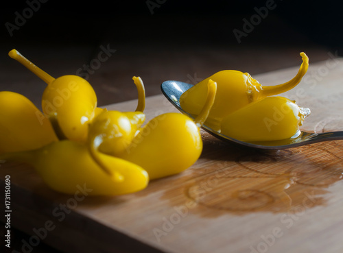 bodefgon fotografico. pepperoncini sobre una cuchara y sobre una tabla de cortar, en una mesa rusticaa de madera con fondo negro. Chile amarillo peque;o