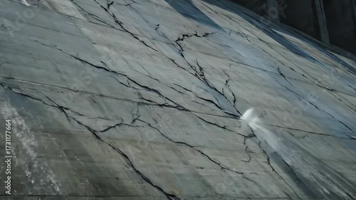 Detailed 4k view reveals extensive cracks and water damage on a gray concrete dam structure, showing the impact of erosion in an industrial landscape.