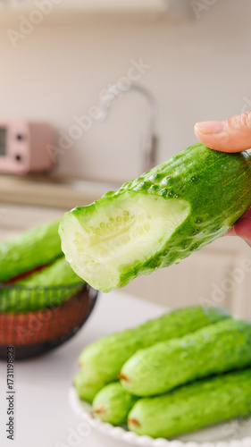 Hand holding fresh sliced green cucumber showing white flesh and seeds in modern kitchen