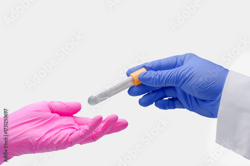 A laboratory technician hands another a venipuncture blood sample tube.