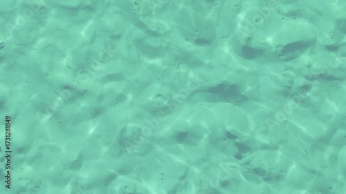 A serene view of clear turquoise water with gentle ripples and sandy textures beneath.