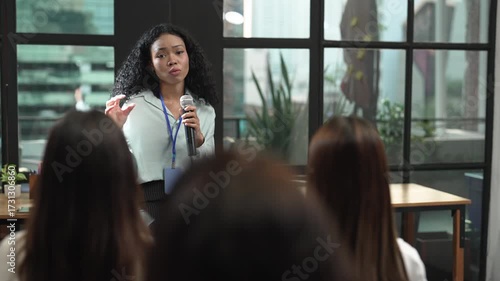 Young African-American woman confidently speaking at a seminar or workshop in a modern office setting. Great for leadership, DEI, education, or public speaking topics.
