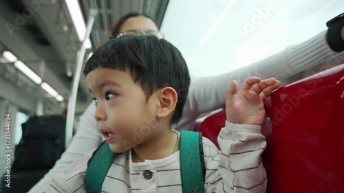 Asian child looking around skytrain with excitement, mother smiling nearby enjoying family travel and happy city ride together
