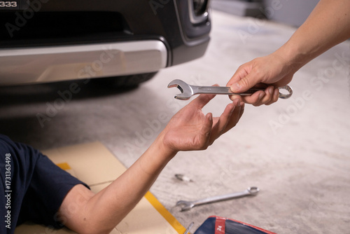 Picture of a young man handing a wrench to an engine repairman.