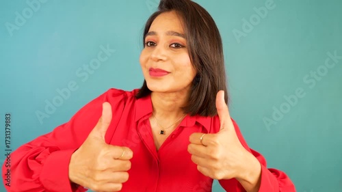 Closeup portrait of happy positive beautiful young woman looking at camera showing thumbs up hands gesture sign well-done like recommend good, isolated over blue background.