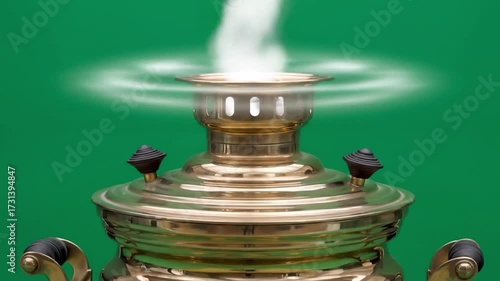 Close-up shot of a traditional brass samovar with steam rising against a green background.