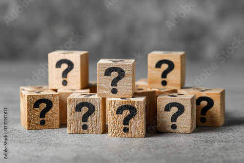 A pile of wooden blocks each with a black question mark symbol representing questions uncertainty and the need for answers or solutions on a gray background