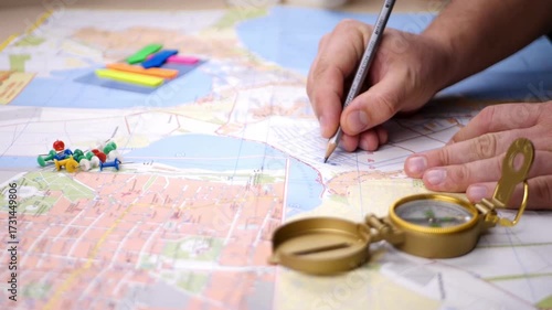 view of a male hand holding a beautiful compass and map as background. searching direction with compass and map. Closeup of hand holding magnetic compass and showing directions.
