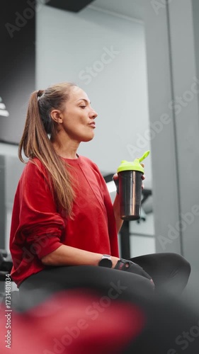 Sporty woman resting in gym with protein shaker in hand. Post workout recovery, hydration, and nutrition for energy and wellness concept of fitness motivation and balance.