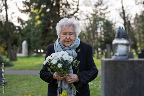 Fotografi Elderly woman visiting a grave on All Saints Day.