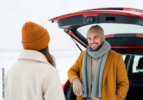 Couple in winter clothing standing by a car in a snowy landscape