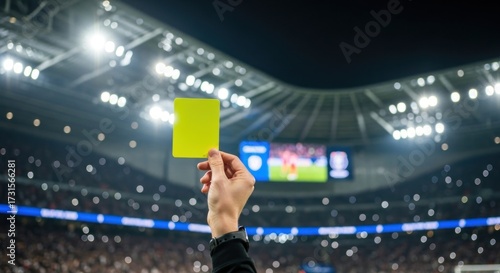 A referee's hand holds up a yellow card during a nighttime soccer match in a stadium.